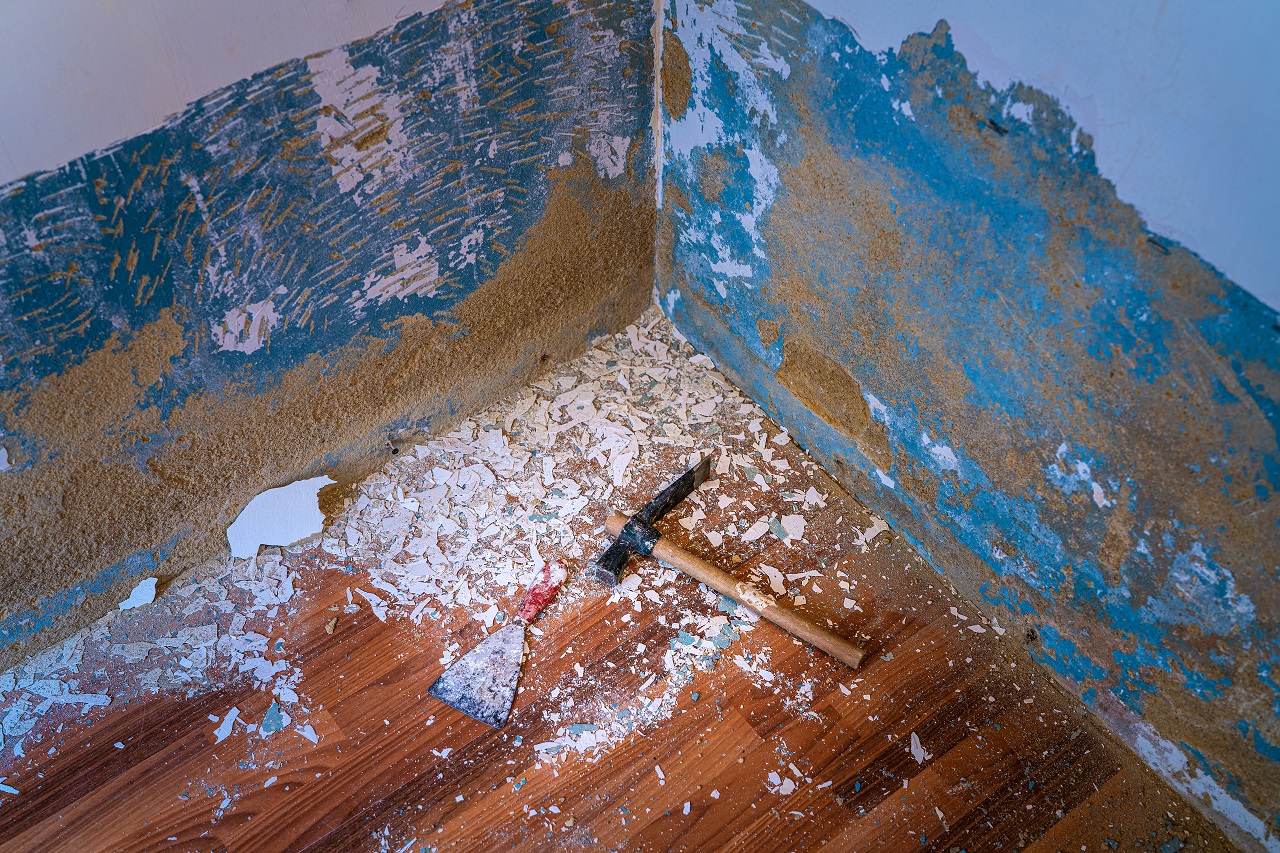 Hammer and scraper on the floor with specks of old paint removed from the wall