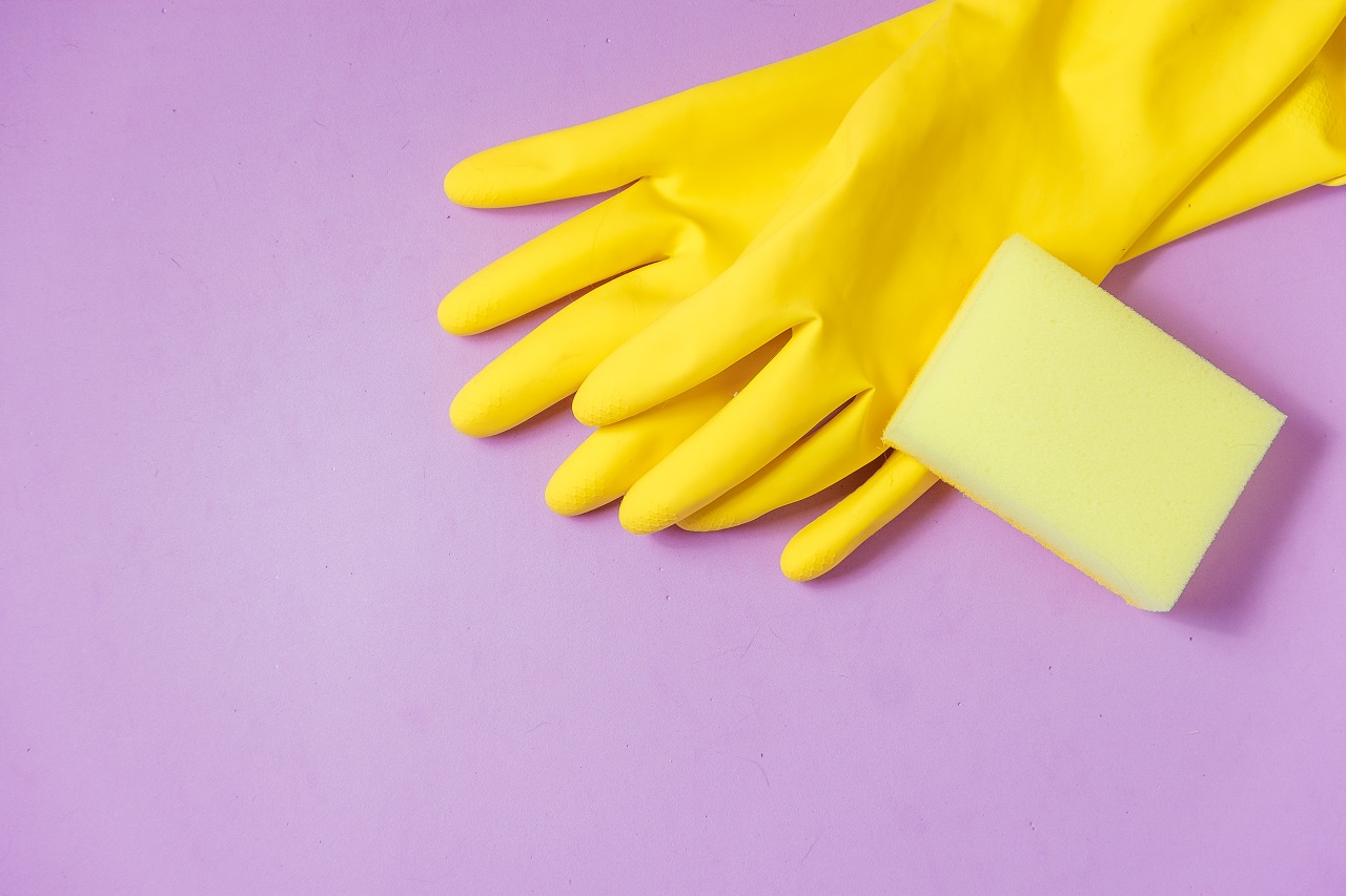 Yellow gloves and a yellow sponge on top of a purple background