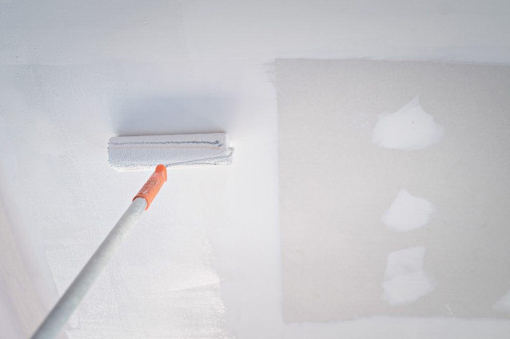 A paint roller painting the ceiling in sections