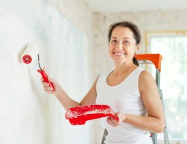 An older woman happily painting a wall