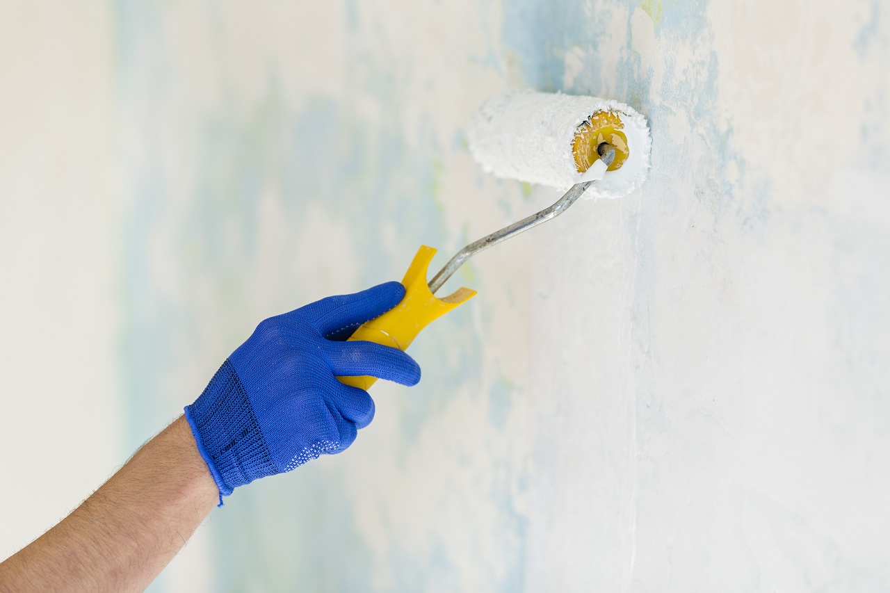 A hand using a roller to paint a wall